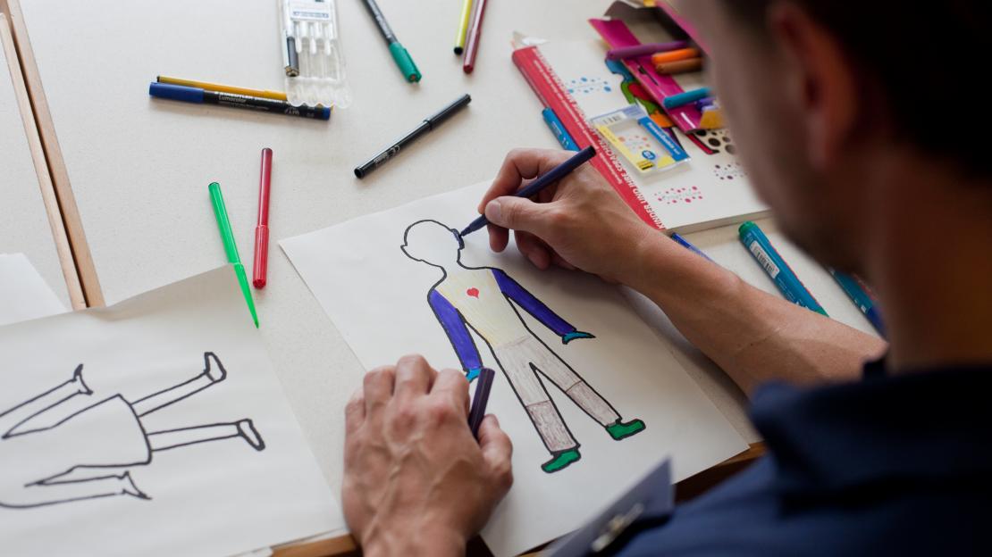 Ein Mann zeichnet eine Figur auf ein Blatt Papier