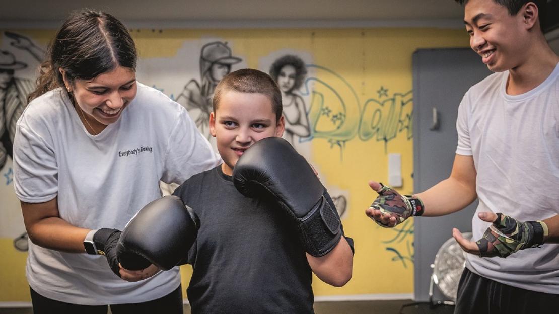 Ein Junge mit Boxhandschuhen wird von einer Trainerin angeleitet