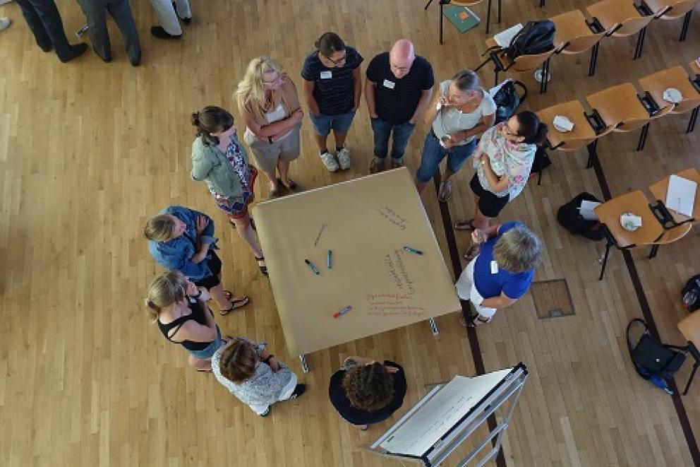 Mehrere Personen stehend um einen Tisch bei einem Workshop